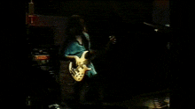 a man in a blue shirt is playing a guitar on a stage