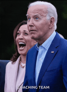 a man in a blue suit stands next to a woman who is laughing and the words coaching team are below him