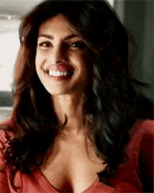 a woman in a red shirt is smiling and wearing a plunging neckline .