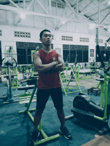 a man in a gym with his arms crossed wearing a red tank top