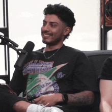 a man wearing a college marathon shirt is smiling in front of a microphone while sitting on a couch .