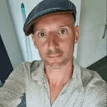 a man wearing a flat cap and a shirt is taking a selfie .