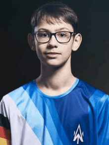 a young man wearing glasses and a blue shirt is standing in front of a dark background .