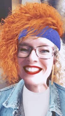 a woman with red hair wearing glasses and a blue headband smiles