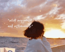 a woman sitting on a beach looking at the ocean with a quote in a foreign language