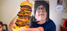 a man with glasses is holding a very tall hamburger in front of his face