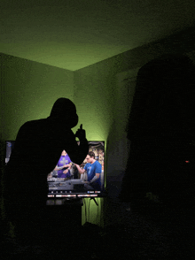 a silhouette of a man standing in front of a tv with a green light behind him