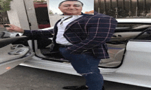 a man in a plaid jacket stands next to a white car