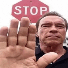 arnold schwarzenegger is giving a high five in front of a stop sign .