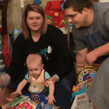 a man and a woman are playing with a baby who is wearing a bib that says teddy bear on it