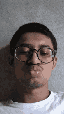 a young man wearing glasses and a white shirt is making a funny face