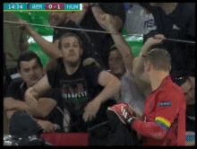 a man in a red shirt with a rainbow sleeve stands in front of a crowd during a soccer game