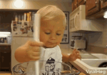 a baby in a cupcake shirt is playing with a stick in a glass bowl with viralhog written on the bottom