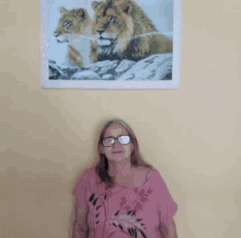 a woman wearing glasses stands in front of a picture of two lions on a wall