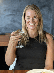 a woman in a black top is holding a martini glass with olives in it