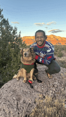 a man wearing a sweater with a reindeer on it kneeling down next to a dog