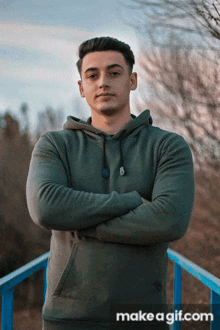 a man in a green hoodie stands with his arms crossed on a blue railing