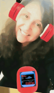 a woman wearing red headphones is smiling while holding a small red device that says radio arturito