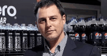 a man in a suit is standing in front of a shelf of pepsi zero bottles .