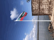 a red white and green flag flies in the wind near a body of water