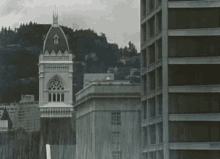 a black and white photo of a city with a large building in the foreground and a clock tower in the background .