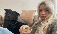 a blonde woman sitting on a couch with a black dog