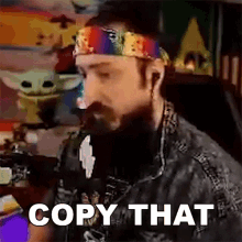 a man with a beard wearing a rainbow headband is sitting in front of a computer and says copy that .