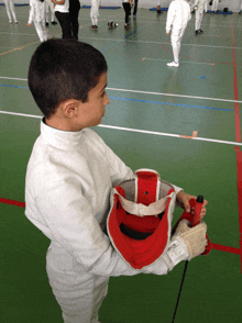 a young boy in a fencing uniform holds a helmet