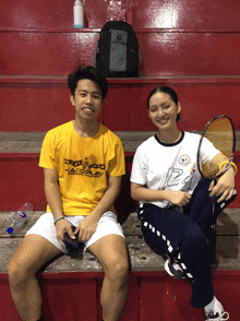 a man and a woman are sitting on a bench and the man is wearing a yellow shirt that says eagle