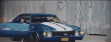 a blue ss muscle car is parked in front of a graffiti covered wall