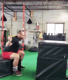 a man squatting on a box in a gym wearing a black shirt that says ' sdp ' on it