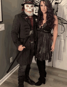 a man wearing a skull mask is standing next to a woman wearing a dress and boots .