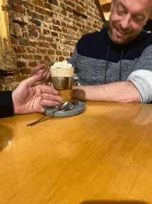 a man sitting at a table with a cup of coffee with whipped cream on top