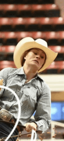 a woman wearing a cowboy hat and striped shirt is holding a rope