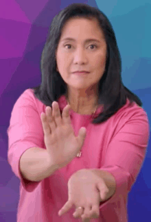 a woman in a pink shirt is making a stop sign with both hands .