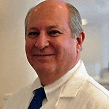 a bald man wearing a white lab coat and blue tie is smiling for the camera .