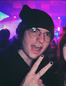 a young man wearing glasses and a black beanie giving a peace sign