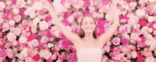 a woman in a white dress is laying in a pile of pink flowers with her arms outstretched .