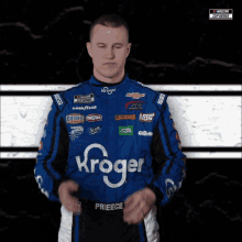 a man wearing a kroger racing suit stands with his eyes closed