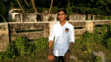 a young man in a white shirt stands in front of a brick wall