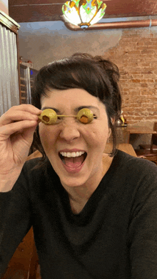 a woman is holding a pair of olives over her eyes