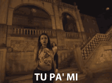 a woman in a floral top is standing in front of a building with the words tu pa ' mi written below her