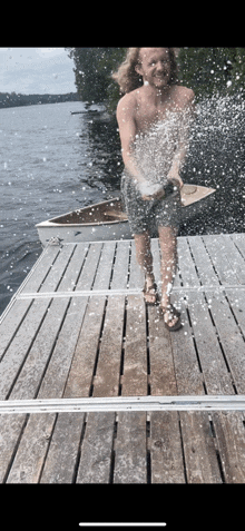 a shirtless man is standing on a dock spraying water at the camera