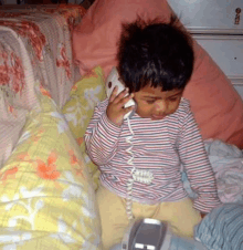 a little boy is sitting on a couch talking on a phone .