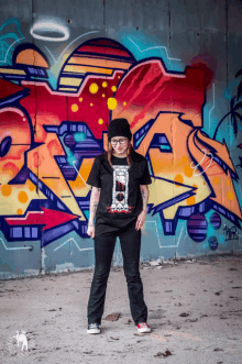 a woman stands in front of a wall with graffiti on it that says ' a ' on it