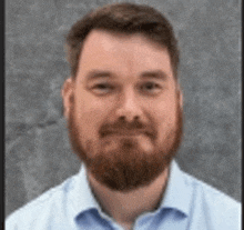 a man with a beard wearing a blue shirt is smiling for the camera .