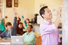 a man in a purple shirt is pointing at a white board in front of a classroom full of students