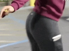 a woman in a burgundy sweatshirt and black leggings is standing on a sidewalk .