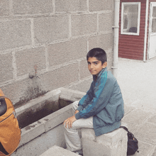 a young boy in a blue adidas jacket sits on a ledge