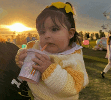 a little girl in a yellow and white sweater drinks from a pink cup with a straw